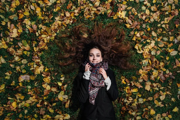 Retrato de una niña tumbada en un césped en un parque forestal. Cabello largo sobre follaje amarillo . — Foto de Stock