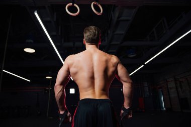 Genç formda adam jimnastik yüzüklerini çekiyor..