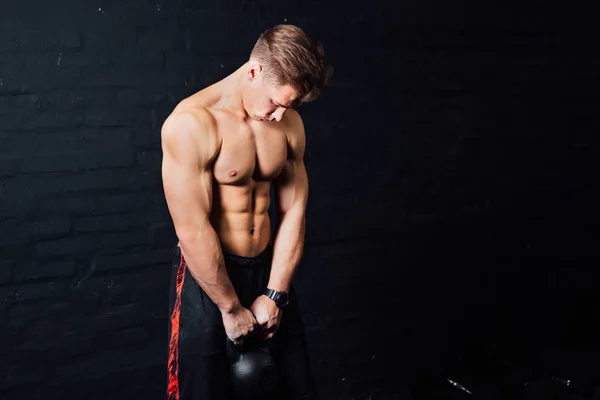 Ung muskulös man träning med kettlebells. mannen med naken överkropp på mörk bakgrund. — Stockfoto