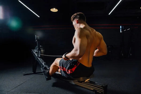 Młody człowiek fitness przy użyciu maszyny do wiosłowania w siłowni — Zdjęcie stockowe