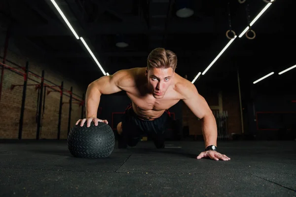 Zelfverzekerde gespierde man doen push up van bal van de geneeskunde in sportschool. — Stockfoto