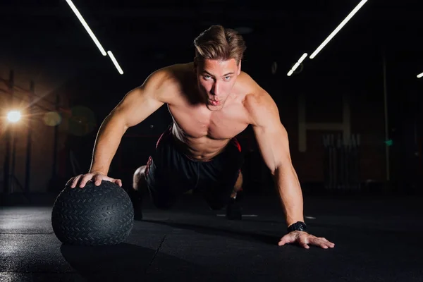 Hombre musculoso confiado haciendo empujar hacia arriba desde la pelota MEDICINE en el gimnasio . — Foto de Stock