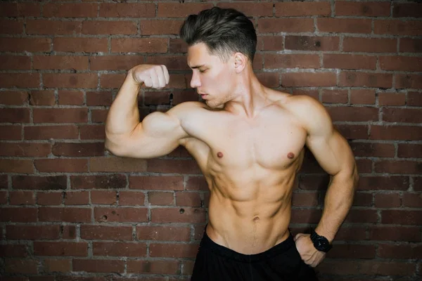 Unga muskulösa bodybuilder fitness modell poserar mot tegel vägg loft och gym. Skönhet ringblixt. — Stockfoto