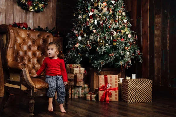 Bir koltuk bir Noel ağacı arka planı sürpriz heyecanlı kız. — Stok fotoğraf