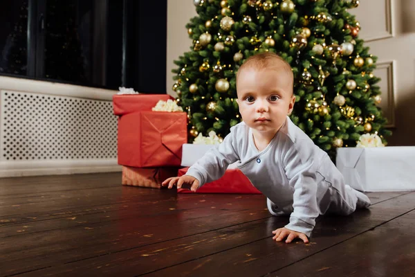 Küçük bebek bir Noel ağacı arka planı kanepede oturuyor. — Stok fotoğraf