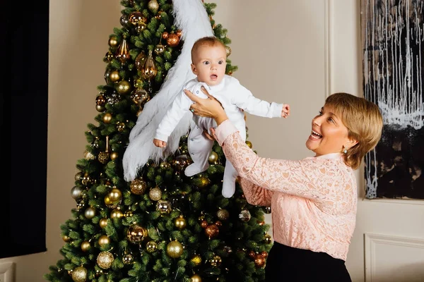 Bir Noel ağacı arka plan üzerinde kollarında bir çocukla zarif büyükanne. — Stok fotoğraf