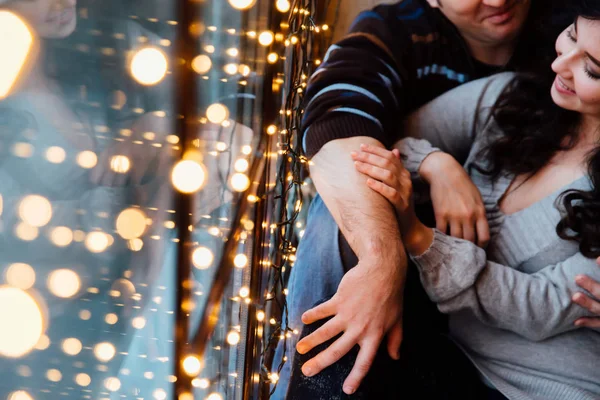 Ζευγάρι των εραστών αγκαλιές κάθεται στο περβάζι στο στούντιο σοφίτα Χριστούγεννα. Τύπος αγκαλιάζει το κορίτσι. — Φωτογραφία Αρχείου