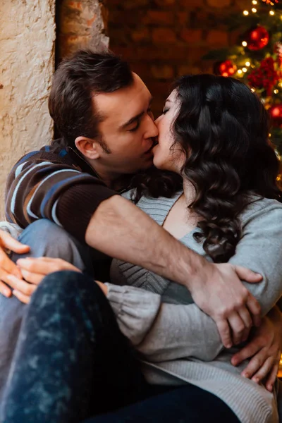 Un paio di amanti si abbracciano seduti sul davanzale dello studio del loft di Natale. ragazzo sta abbracciando la ragazza . — Foto Stock