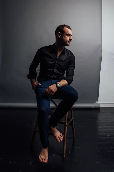 Portret przystojny modne mężczyzna w czarnej koszulce, siedzi na krześle w loft studio fotografii. — Zdjęcie stockowe