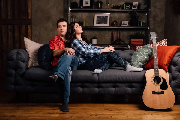 Çift kanepede bir gitar ile oturuyor. Uzun saçlı esmer bir akustik gitar ile. — Stok fotoğraf