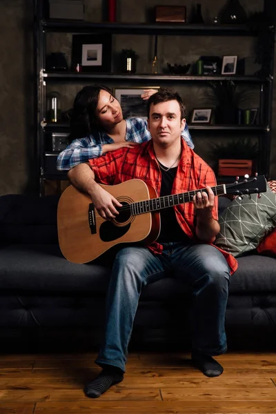 Çift kanepede bir gitar ile oturuyor. Uzun saçlı esmer bir akustik gitar ile. — Stok fotoğraf