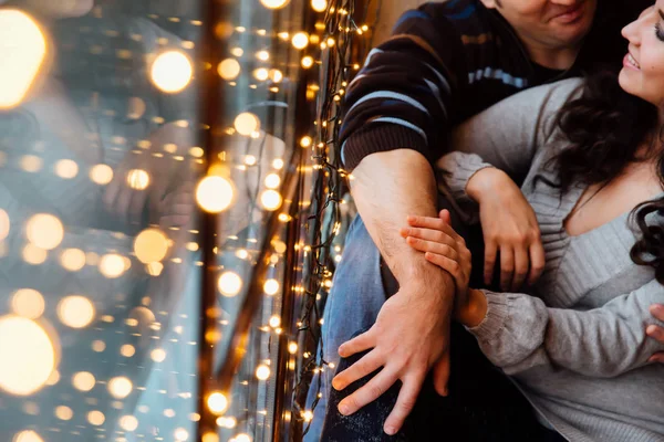 Ζευγάρι των εραστών αγκαλιές κάθεται στο περβάζι στο στούντιο σοφίτα Χριστούγεννα. Τύπος αγκαλιάζει το κορίτσι. — Φωτογραφία Αρχείου