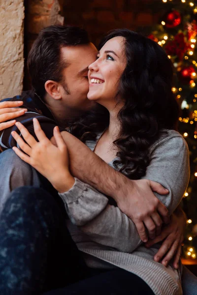 Paar liefhebbers hugs zittend op de vensterbank in de kerst loft studio. Guy is knuffelen het meisje. — Stockfoto