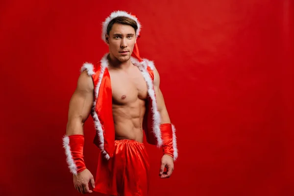 Vánoční svátky. sexy silné santa claus klobouk. Svalnatý mladík. červené pozadí. — Stock fotografie