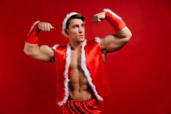 Christmas holidays. sexy strong santa claus wearing hat. Young muscular man. red background. — Stock Photo, Image