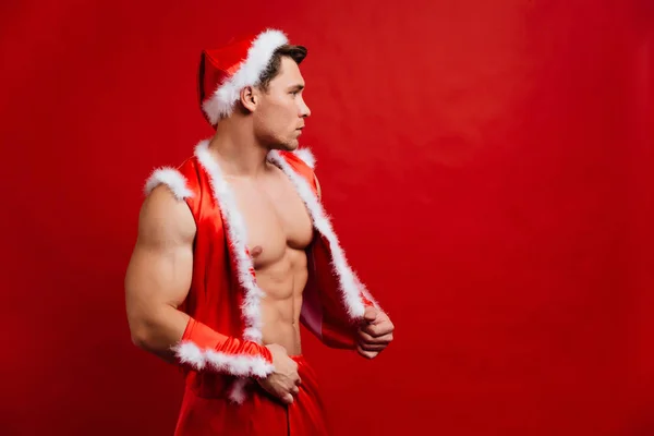 Christmas holidays. sexy strong santa claus wearing hat. Young muscular man. red background. — Stock Photo, Image