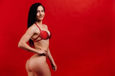 güzel genç kız fitness modeli kırmızı arka planda seksi sutyen duruyor.