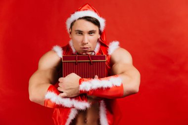 Tatil kutlamaları, yılbaşı, yılbaşı. Seksi fitness Noel Baba şapkalı bir hediye kutusu tutuyor.