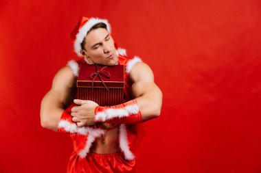 Tatil kutlamaları, yılbaşı, yılbaşı. Seksi fitness Noel Baba şapkalı bir hediye kutusu tutuyor.