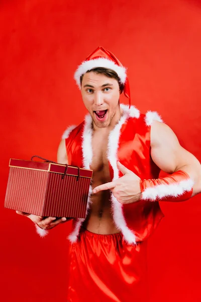 Svátky oslavy, Silvestr, Vánoce. Sexy fitness Santa Claus v klobouku je drží dárková krabička. — Stock fotografie