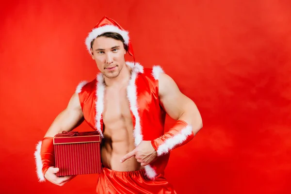 Holidays celebrations, New year, Christmas. Sexy fitness Santa Claus in a hat is holding a gift box. — Stock Photo, Image