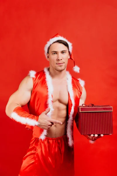 Svátky oslavy, Silvestr, Vánoce. Sexy fitness Santa Claus v klobouku je drží dárková krabička. — Stock fotografie
