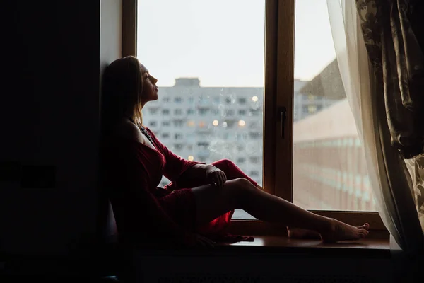 Красивая сексуальная девушка в красном халате сидит дома на подоконнике . — стоковое фото