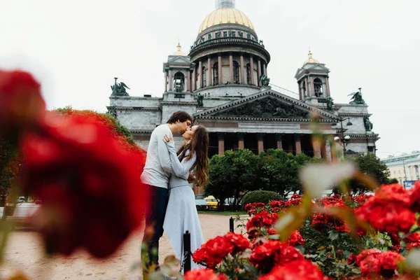 Любляча пара обіймається на тлі червоних квітів і старовинної архітектури . — стокове фото