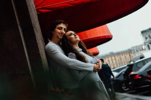 Een verliefde paar hugs onder het bladerdak van de rode winkel op straat. Omarmen. — Stockfoto