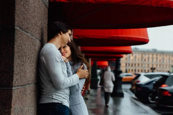 Una coppia amorevole abbraccia sotto il baldacchino del negozio rosso per strada. Abbracciare . — Foto Stock