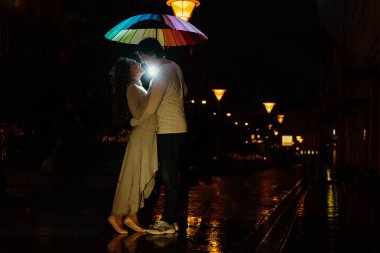 genç bir çift bir şemsiye altında geceleri bir şehir sokak öper..