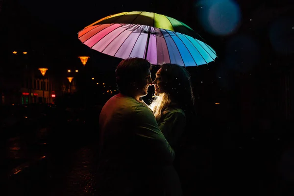 Mladý pár pod slunečníkem polibky v noci ve městě. — Stock fotografie