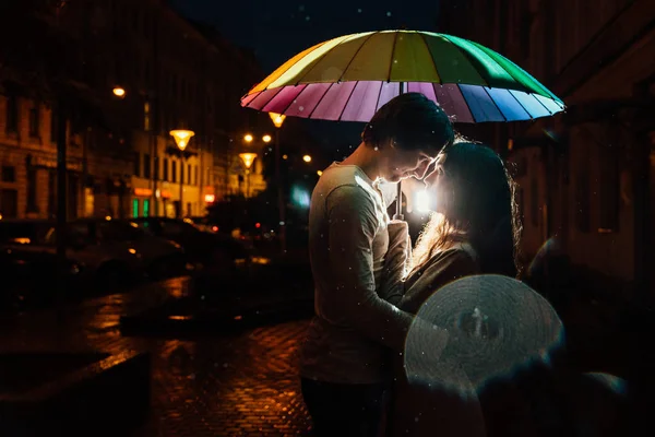 Jovem casal sob um guarda-chuva beijos à noite em uma rua da cidade . — Fotografia de Stock