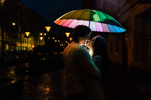 Jeune couple sous un parapluie embrasse la nuit dans une rue de la ville . — Photo