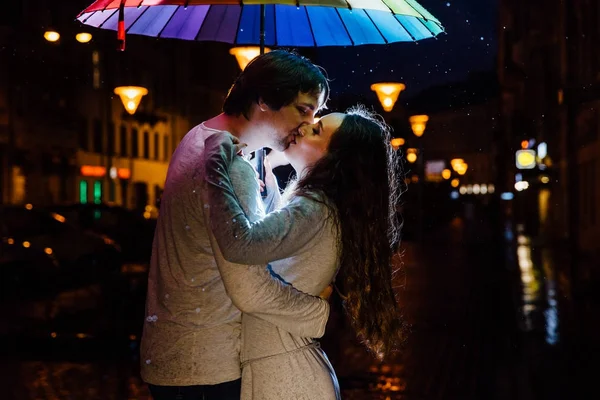 Jeune couple sous un parapluie embrasse la nuit dans une rue de la ville . — Photo
