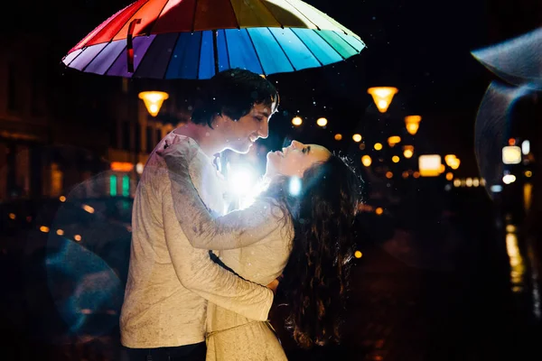 Jovem casal sob um guarda-chuva beijos à noite em uma rua da cidade . — Fotografia de Stock