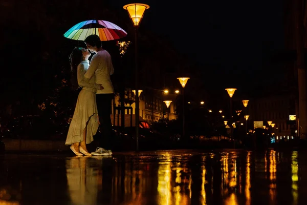 Νεαρό ζευγάρι κάτω από μια ομπρέλα φιλιά το βράδυ σε ένα δρόμο της πόλης. — Φωτογραφία Αρχείου