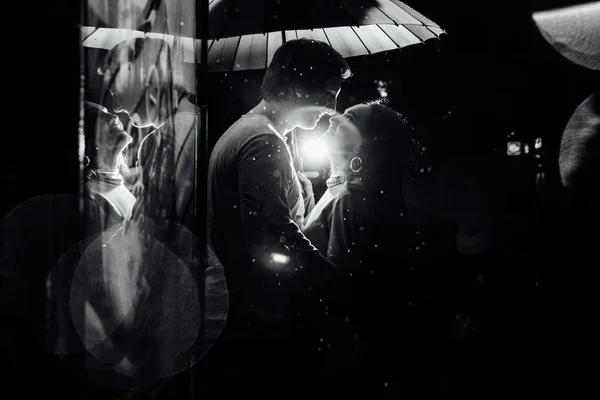 Joven pareja bajo un paraguas besos en la noche en una calle de la ciudad . — Foto de Stock