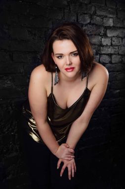 artı boyutu model altın bir bluz ve tuğla loft arka plan üzerinde siyah kot.