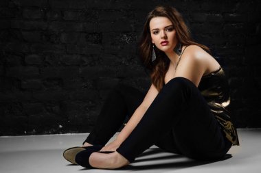 artı boyutu model altın bir bluz ve tuğla loft arka plan üzerinde siyah kot.