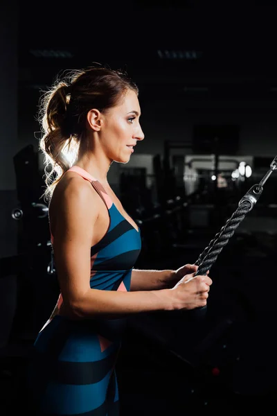 Atleta mujer hace un tríceps en el bloque en el simulador de cruce en el gimnasio . —  Fotos de Stock