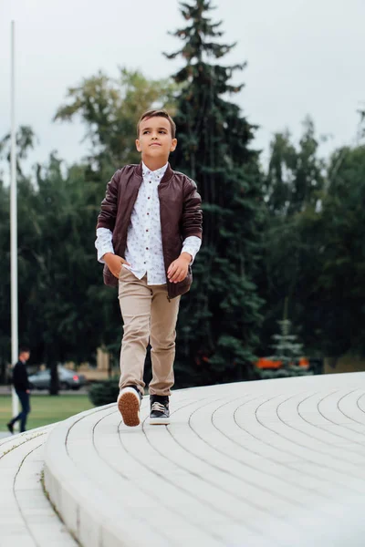 Kahverengi deri ceket giyen bir şehirde, merdivenlerde oturan sevimli küçük çocuk. — Stok fotoğraf