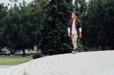 Kahverengi deri ceket giyen bir şehirde, merdivenlerde oturan sevimli küçük çocuk.