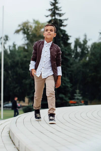 Adorable petit garçon assis dans les escaliers d'une ville, vêtu d'une veste en cuir marron . — Photo