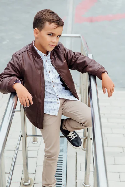 Adolescent garçon attend les escaliers à la rampe. Enfant à la mode dans des vêtements de ville élégants . — Photo