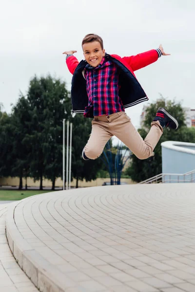 Kahverengi deri ceket giyen bir şehirde, merdivenlerde havada atlama sevimli küçük çocuk — Stok fotoğraf