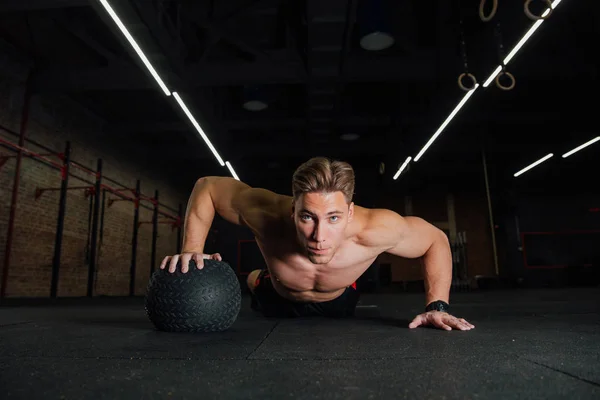 Zelfverzekerde gespierde man doen push up van bal van de geneeskunde in sportschool. — Stockfoto