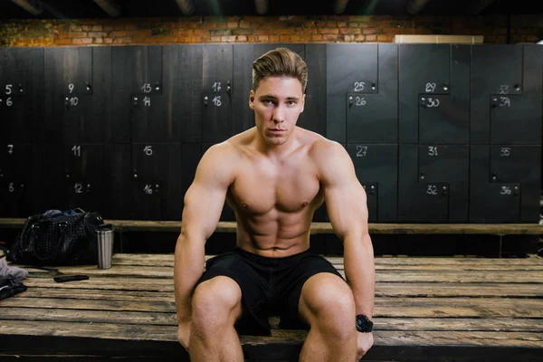 Allvarliga fitness modell av en bodybuilder manliga tränare som sitter på en bänk i omklädningsrummet. — Stockfoto