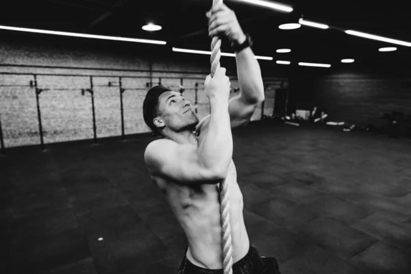 Fitness A erkek atlet spor salonunda bir ip tırmanıyor. Koyu arka plan, çatı. — Stok fotoğraf