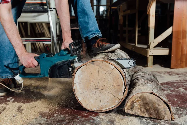 Snickare i verkstaden sågar trädet med en elektrisk motorsåg. snickare i processen för sågning. — Stockfoto